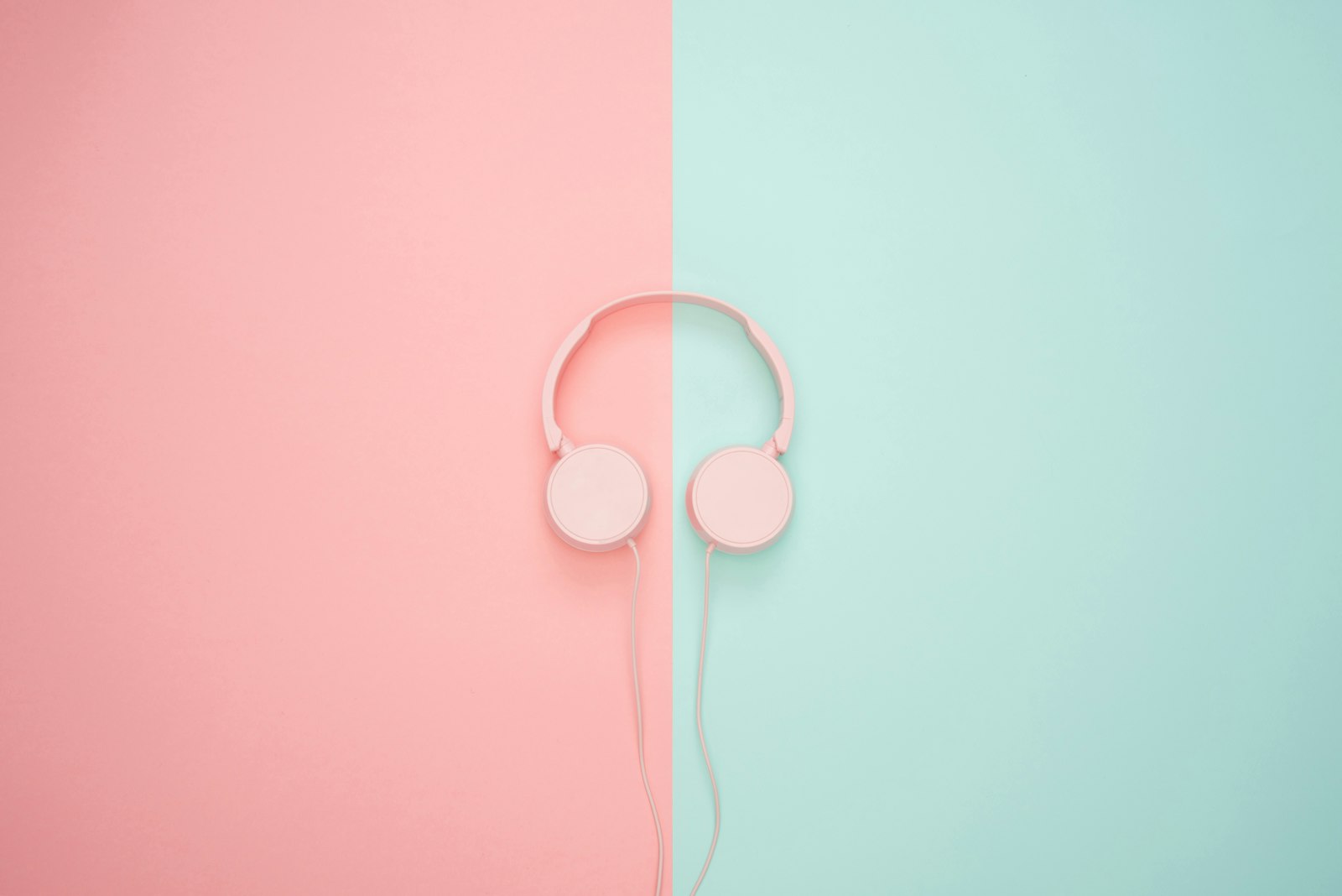 Small pink on-ear headphones with thin pads on a pink and mint background.